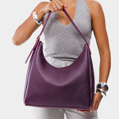 Plum*Large | Model holding u-shaped, flat-bottomed leather shoulder bag with adjustable strap