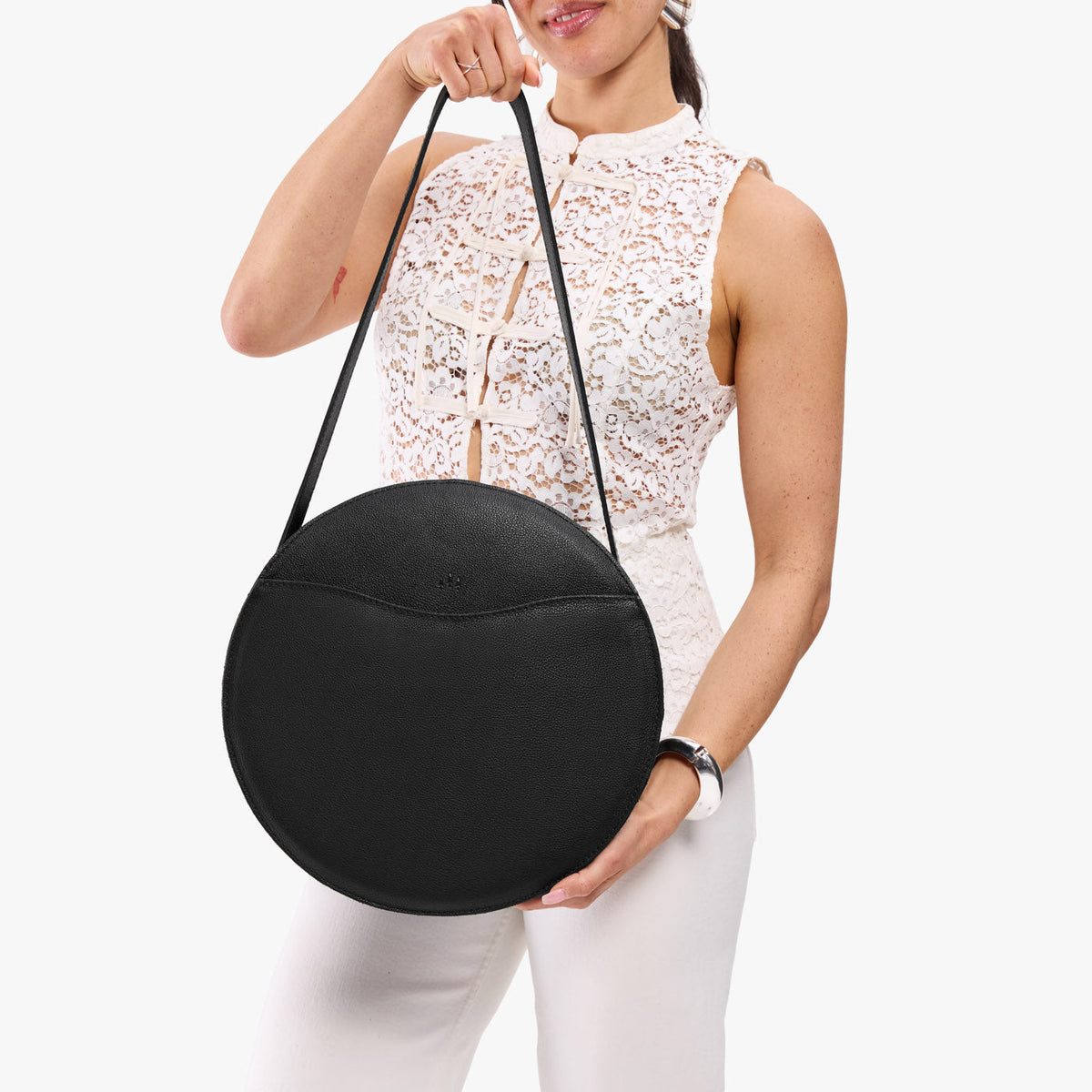 Pebbled--black | Model holding large circle shaped leather bag with top zipper and carrying strap