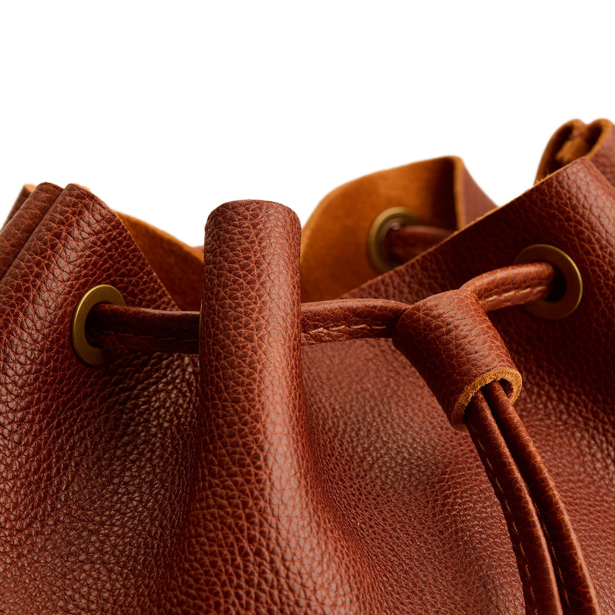 Nutmeg | Close-up of a brown leather drawstring backpack with grommets.