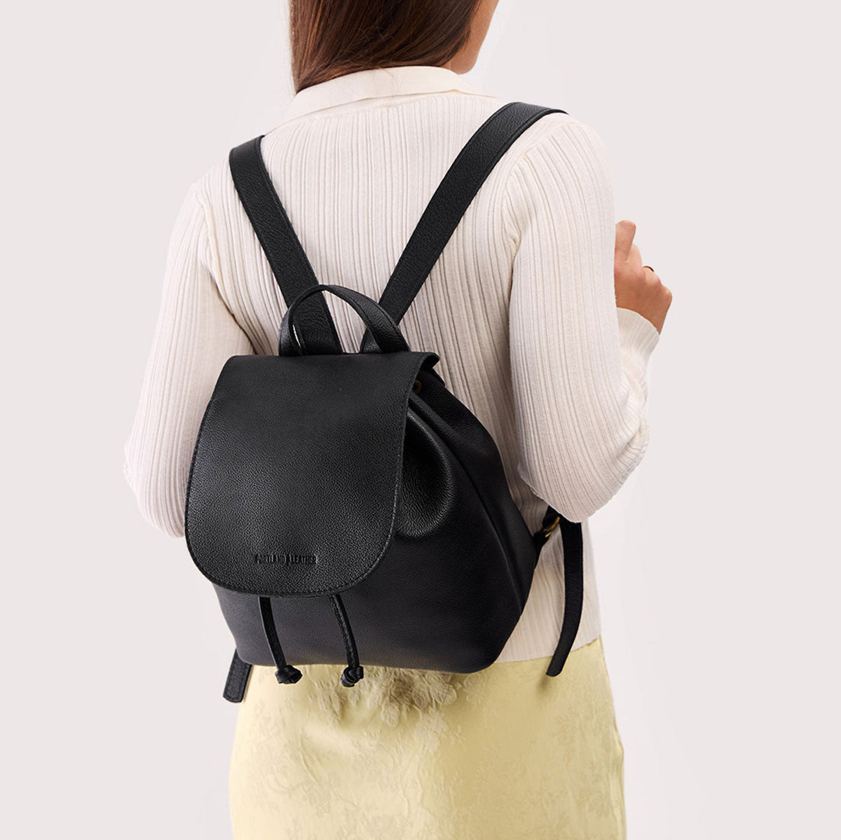 Pebbled--Black | Pebbled black leather drawstring backpack being worn by a person wearing a white sweater.