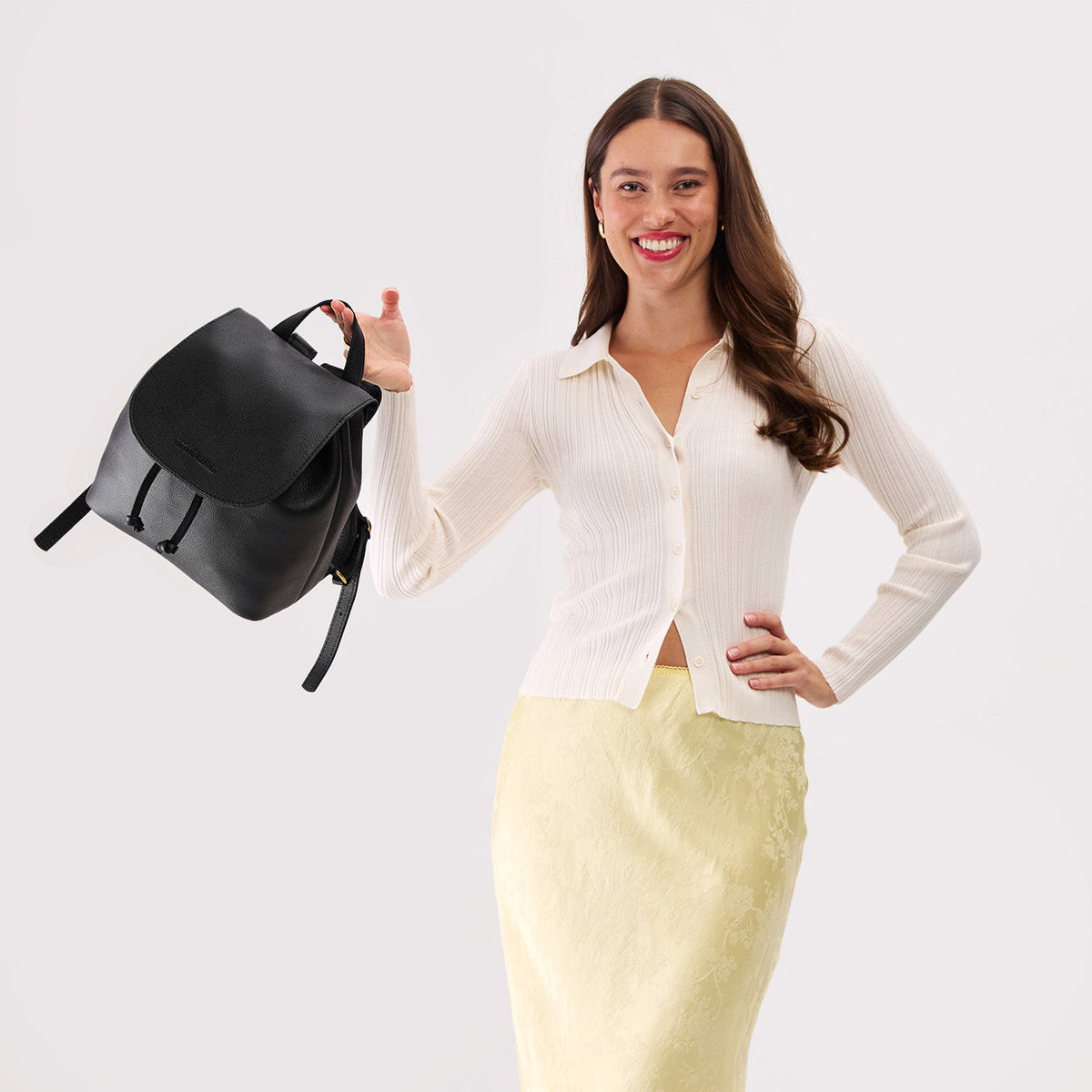 Pebbled--Black | Pebbled black leather drawstring backpack held by a person wearing a white sweater.