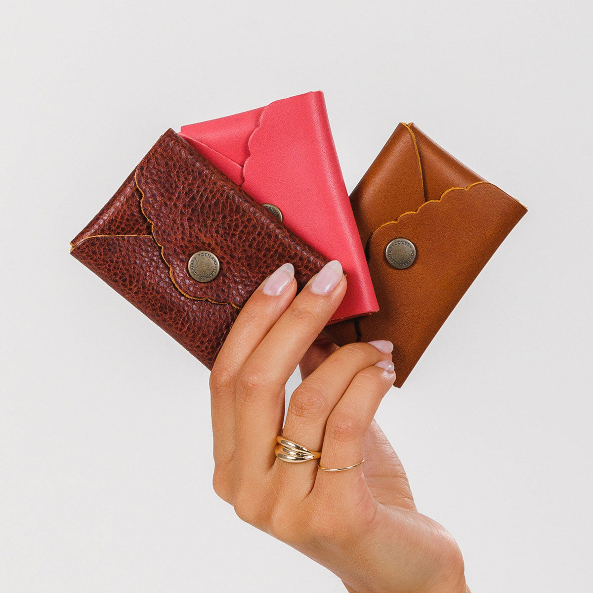All Variants | Hand holding three small leather wallets with scalloped edges