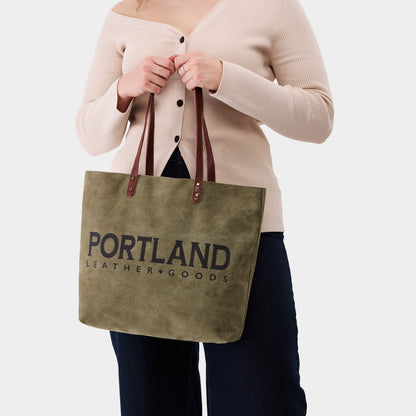 Person holding a green canvas tote bag with 'Portland Leather Goods' branding.