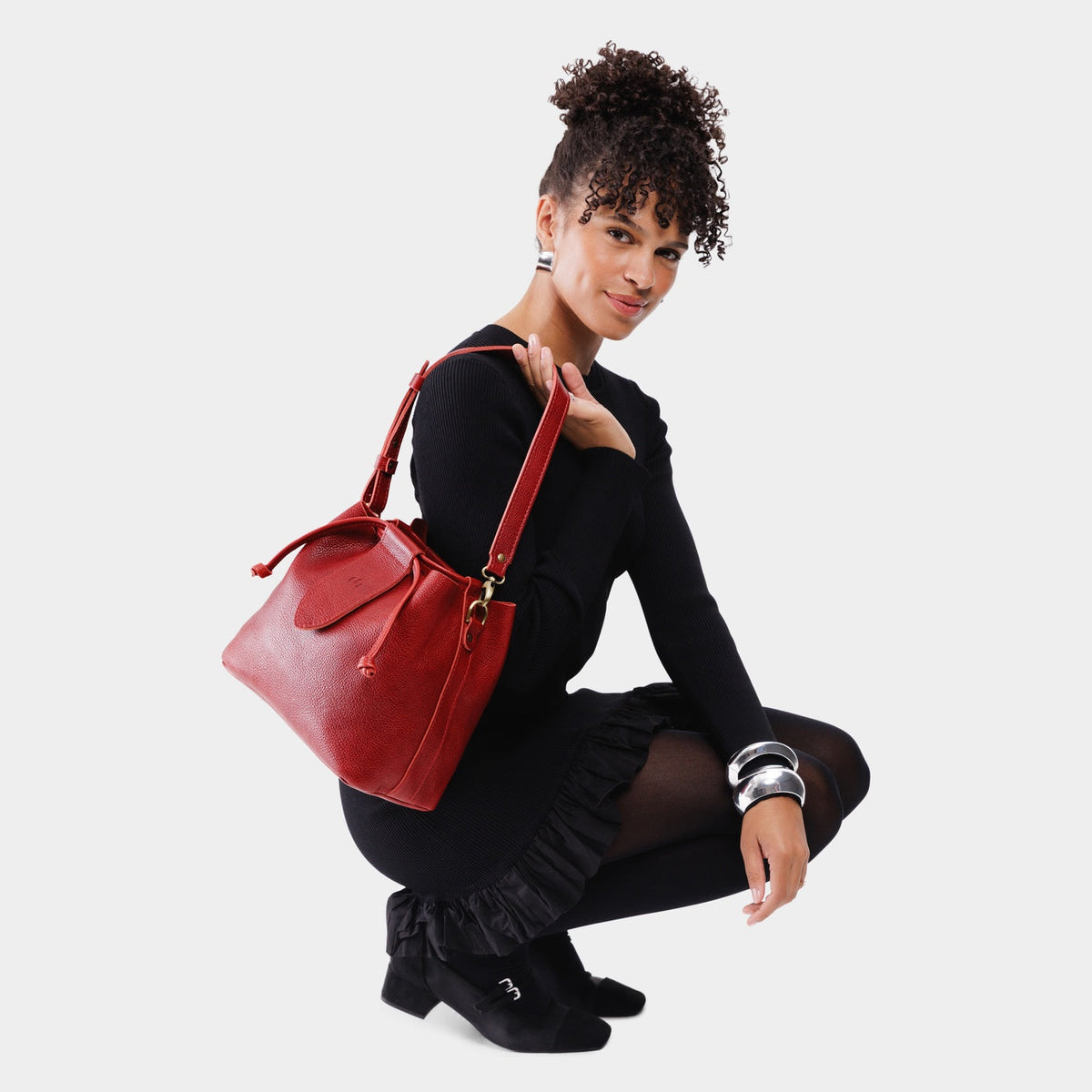 Chili Red*Large | Model holding symmetrical leather bag with leather drawstring closure and adjustable shoulder strap