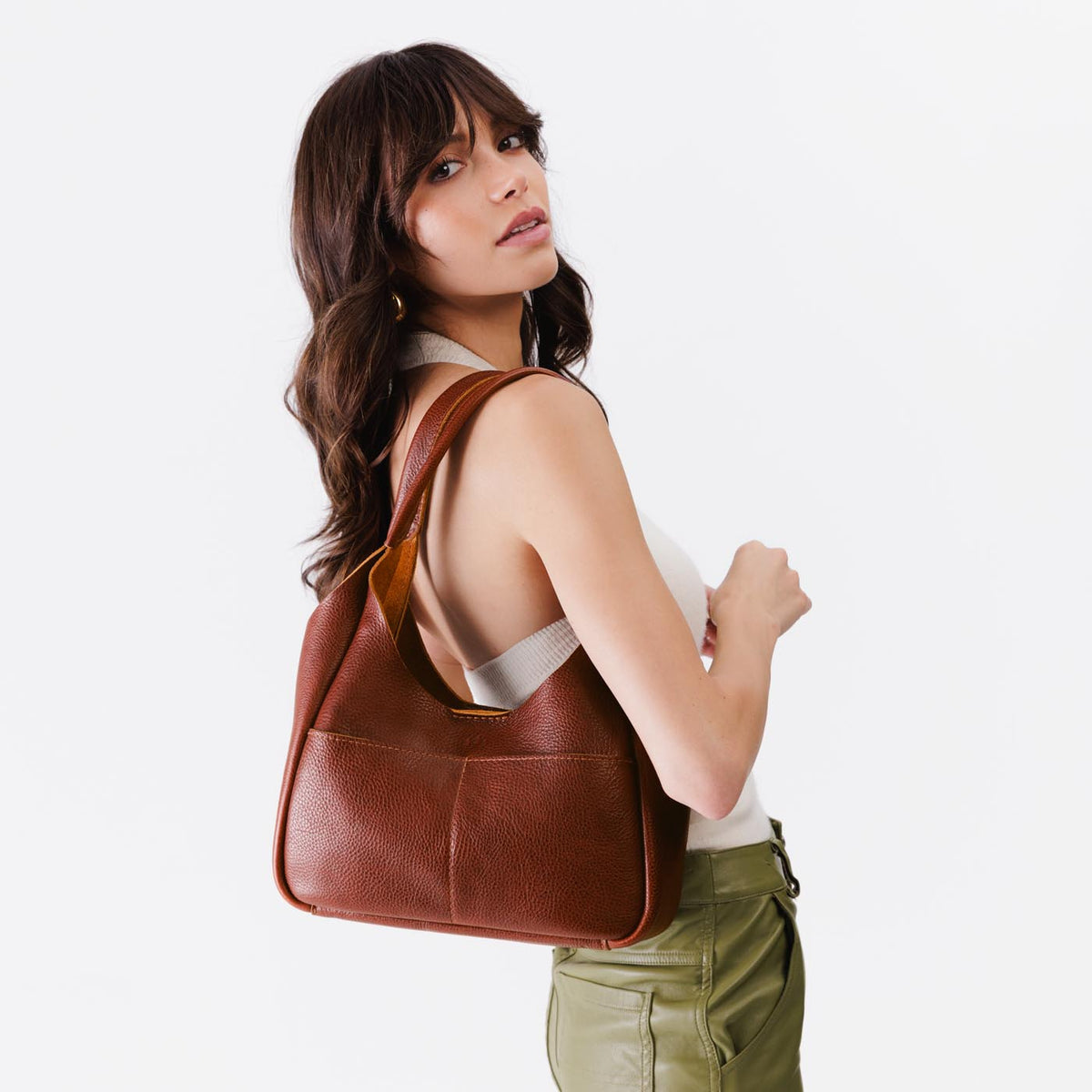 Nutmeg*Medium | A model holding a u-shaped, flat-bottomed leather shoulder bag with two outside pockets