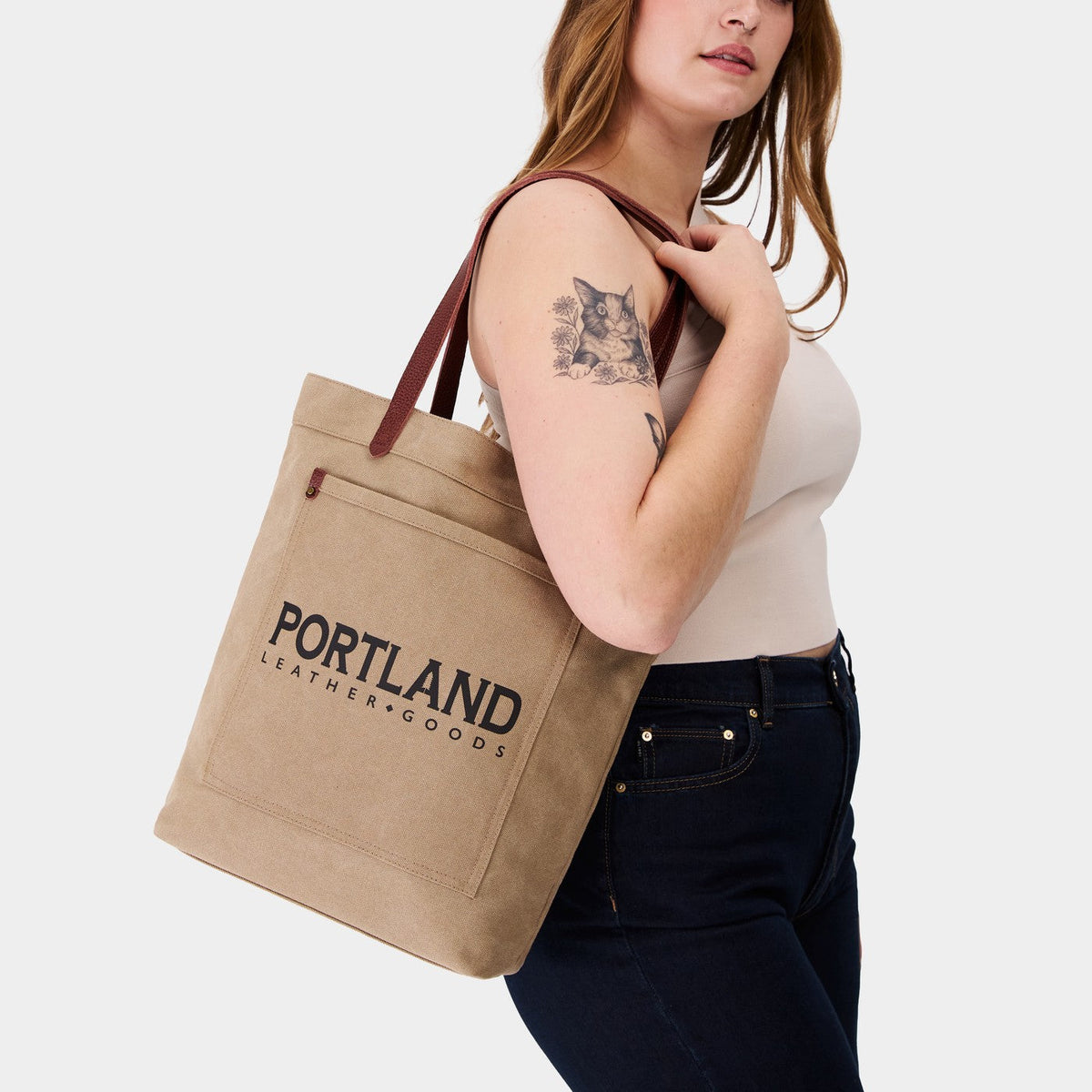 Woman holding a canvas tote bag with 'Portland Leather Goods' branding.