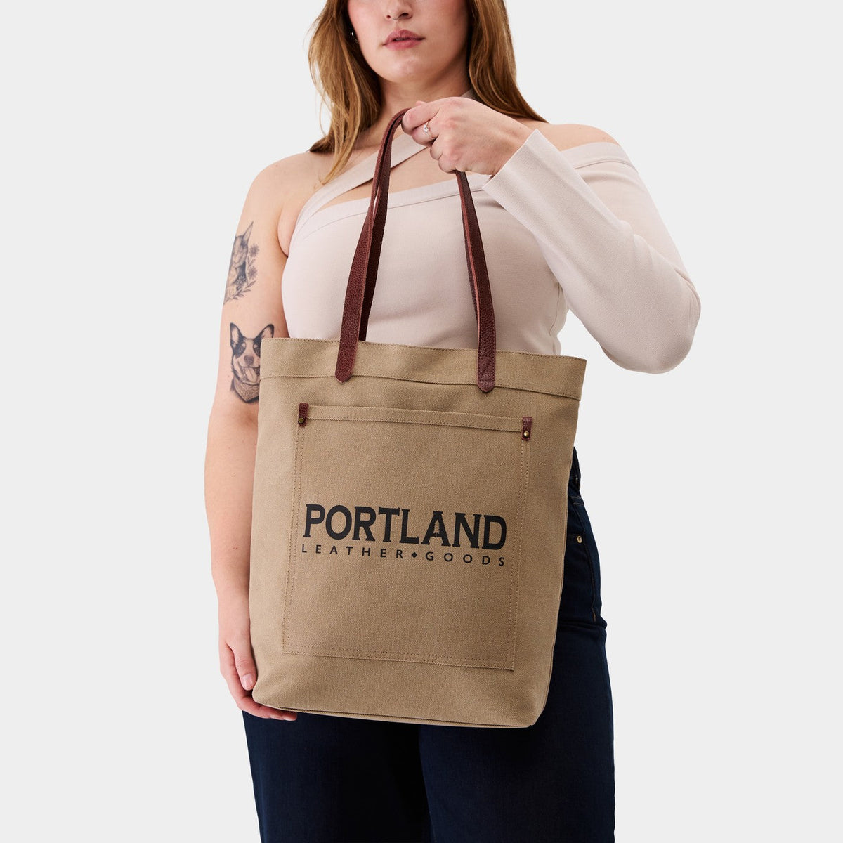 Woman holding a canvas tote bag with 'Portland Leather Goods' branding.